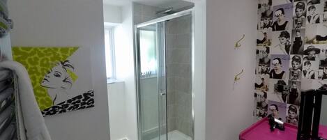 Une salle de bain moderne avec une douche à parois de verre, un meuble-lavabo rose et un mur décoré de photographies en noir et blanc.