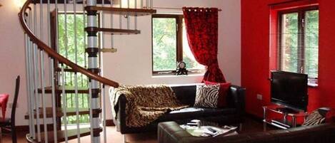 A living room with a spiral staircase, a black leather sofa, a television, and a red wall.