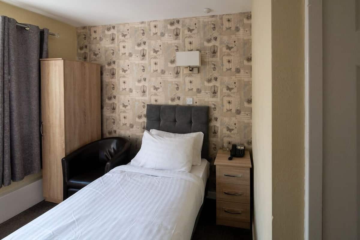 Quarto de hotel com cama, escrivaninha, cadeira, guarda-roupa e papel de parede estampado.
