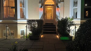 Entrada de un hotel con mostrador de recepción, una escalera y plantas en macetas.
