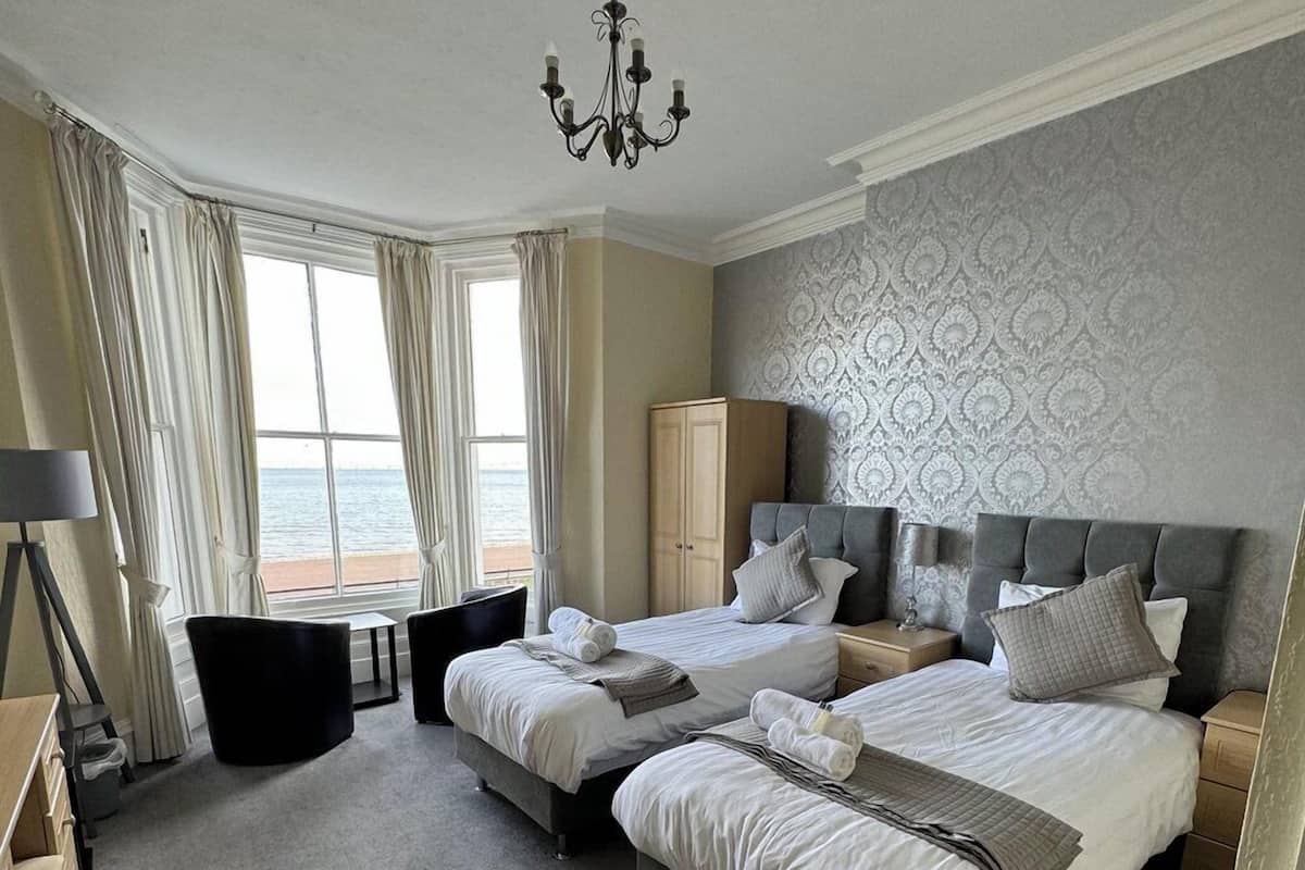 Quarto de hotel com duas camas, um candelabro, vista para o mar e parede estampada.