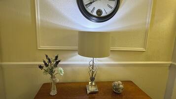 Una mesa de madera con un reloj, un florero con flores y una lámpara.