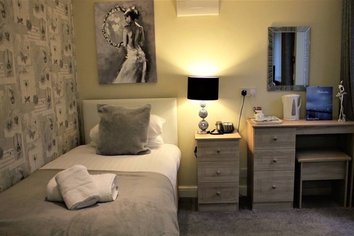 Quarto de hotel com cama, mesa de cabeceira, escrivaninha e espelho.