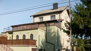 A two-story building with a balcony on the upper floor, a staircase on the lower level, and a fence surrounding the property. - Domowe Spanie (Lomza)