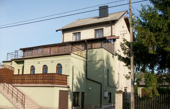 A two-story building with a balcony on the upper floor, a staircase on the lower level, and a fence surrounding the property. - Domowe Spanie (Lomza)