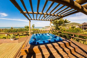 A wooden deck with a hot tub, overlooking a beach and ocean.