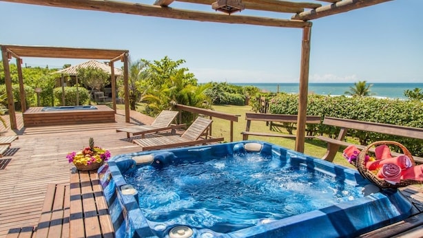 Una terraza de madera con un jacuzzi, sillas de descanso y vista al océano.