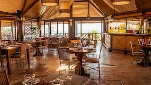 Un restaurante espacioso con techos altos, mesas y sillas de madera, que cuenta con una zona de bar con botellas y vistas al exterior.