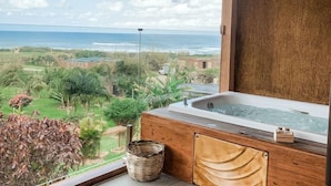 Un baño con bañera de hidromasaje, muebles de madera y vistas al océano y follaje.