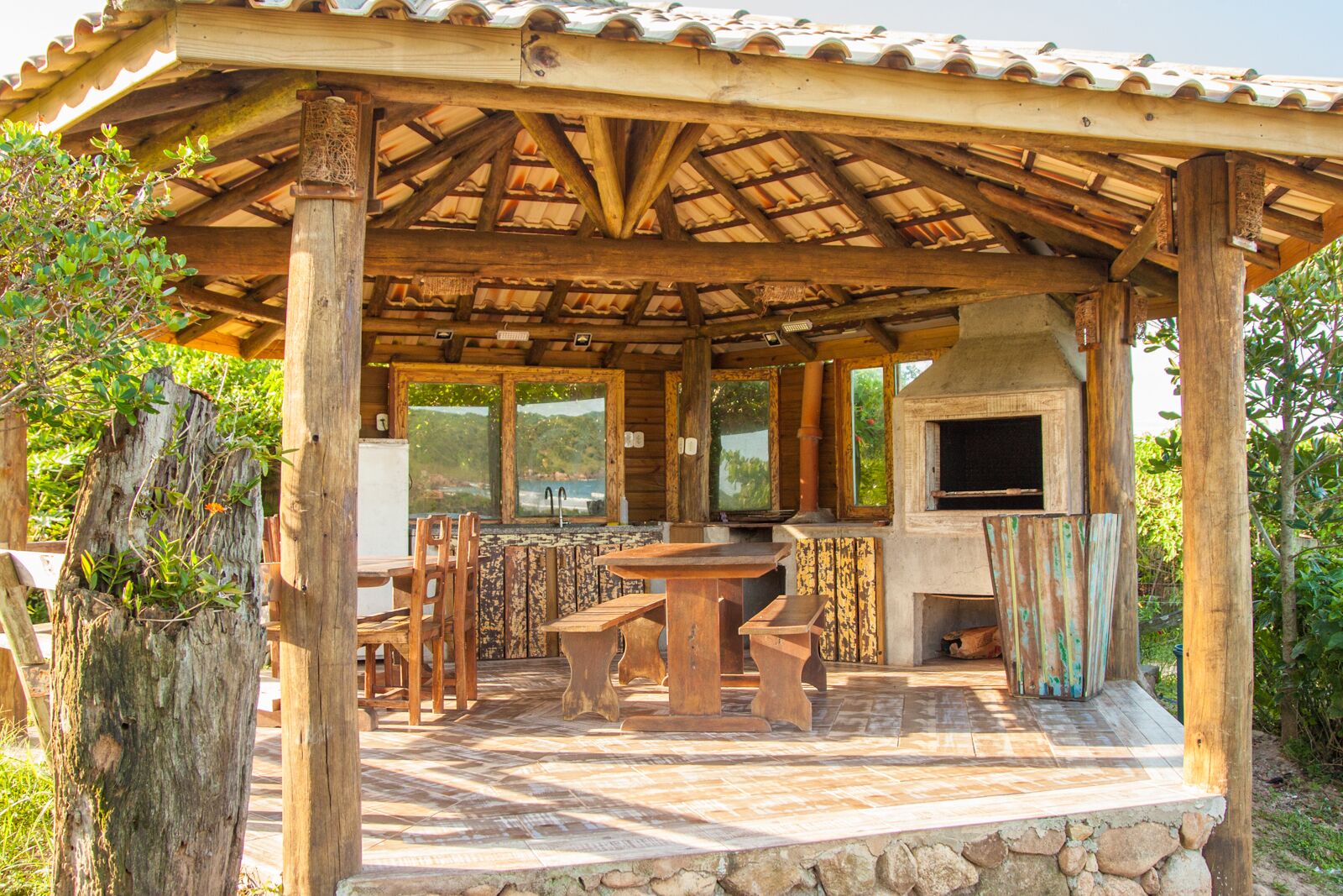 Une cuisine d’extérieur rustique, dotée d’un plan de travail en pierre, de chaises en bois et d’un four encastré.
