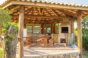 A rustic outdoor kitchen with a stone countertop, wooden chairs, and a built-in oven.