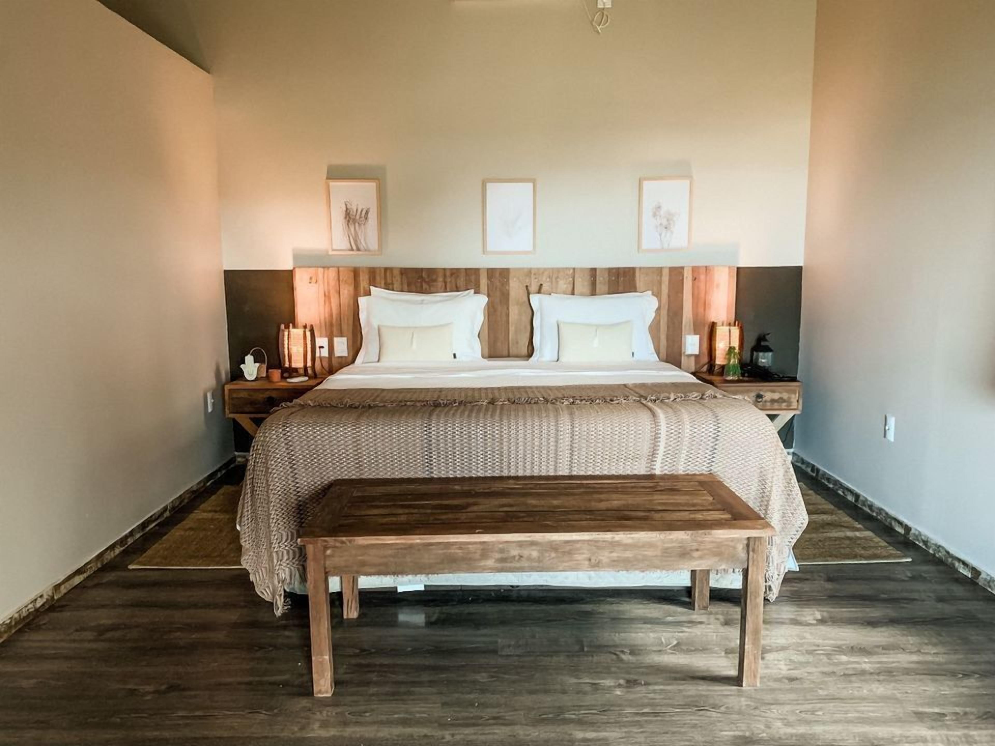 A large bed with a wooden headboard, two bedside tables, and a bench in front of the bed.