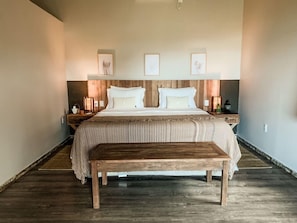 A large bed with a wooden headboard, two bedside tables, and a bench in front of the bed.