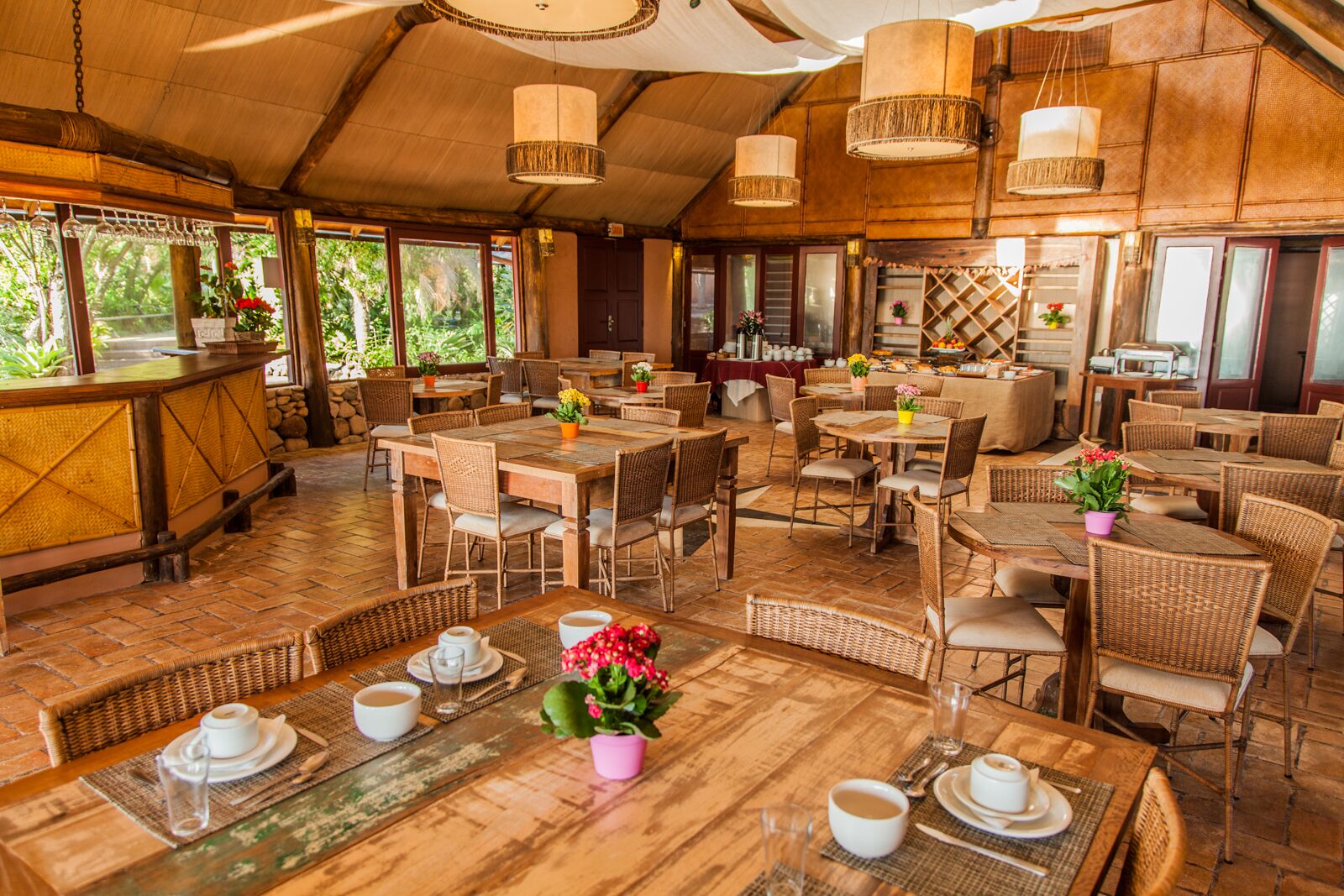 Ein Restaurant im Freien mit Holztischen und -stühlen, Blumentöpfen und hängenden Lampen.