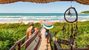 Un sendero de madera que conduce a una playa con una estructura de techo de paja.