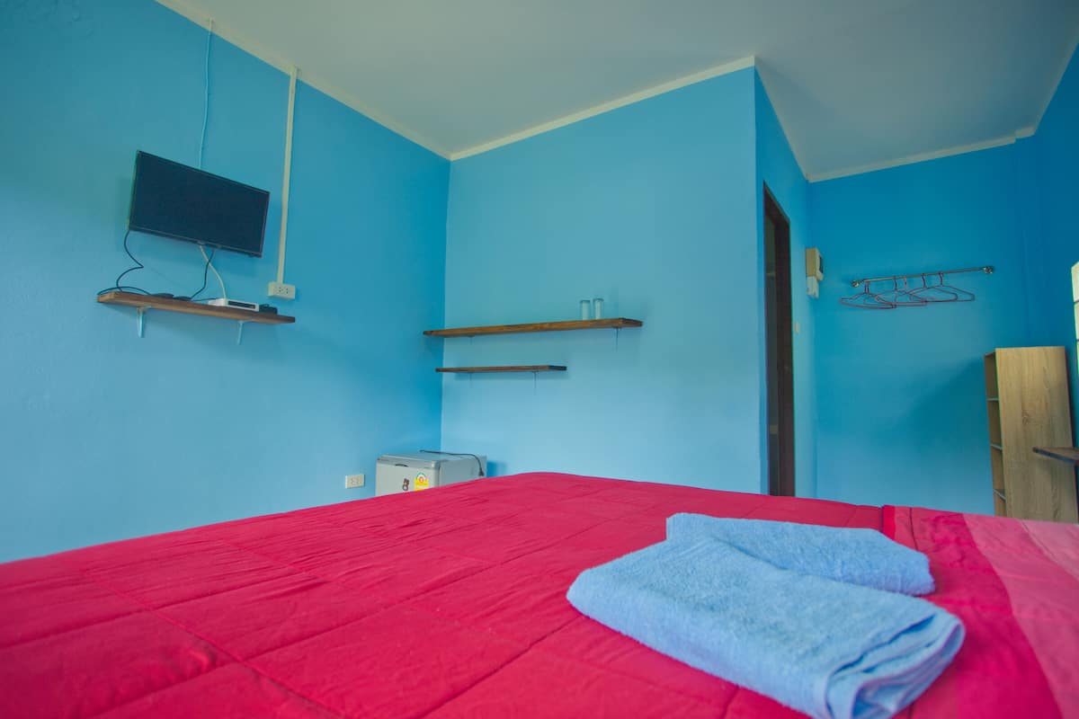 Quarto com cama, televisão na parede e um pequeno armário.