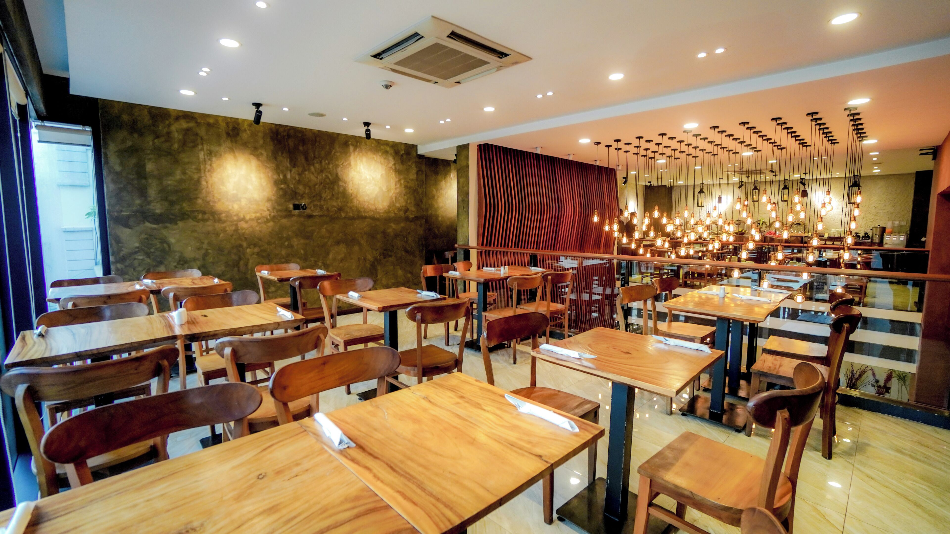 L’intérieur d’un restaurant avec des tables et des chaises en bois, un mur orné de motifs et des lampes suspendues.