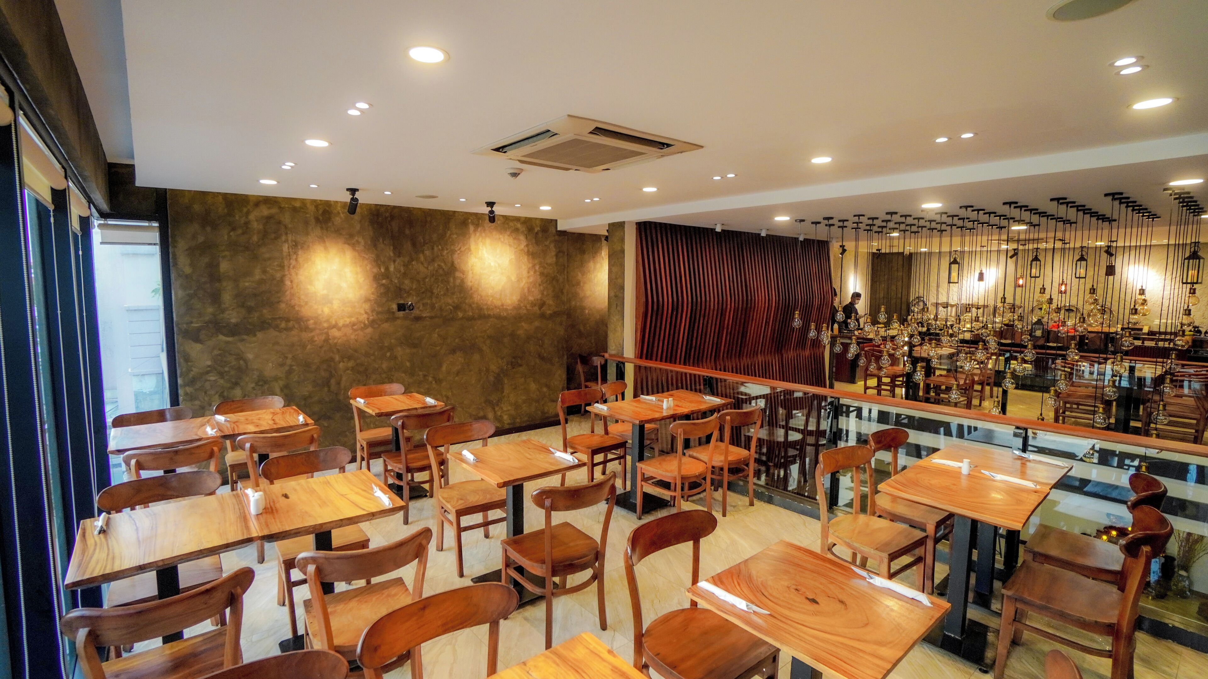 A restaurant interior with wooden tables and chairs, a bar area with hanging light fixtures, and a textured wall.