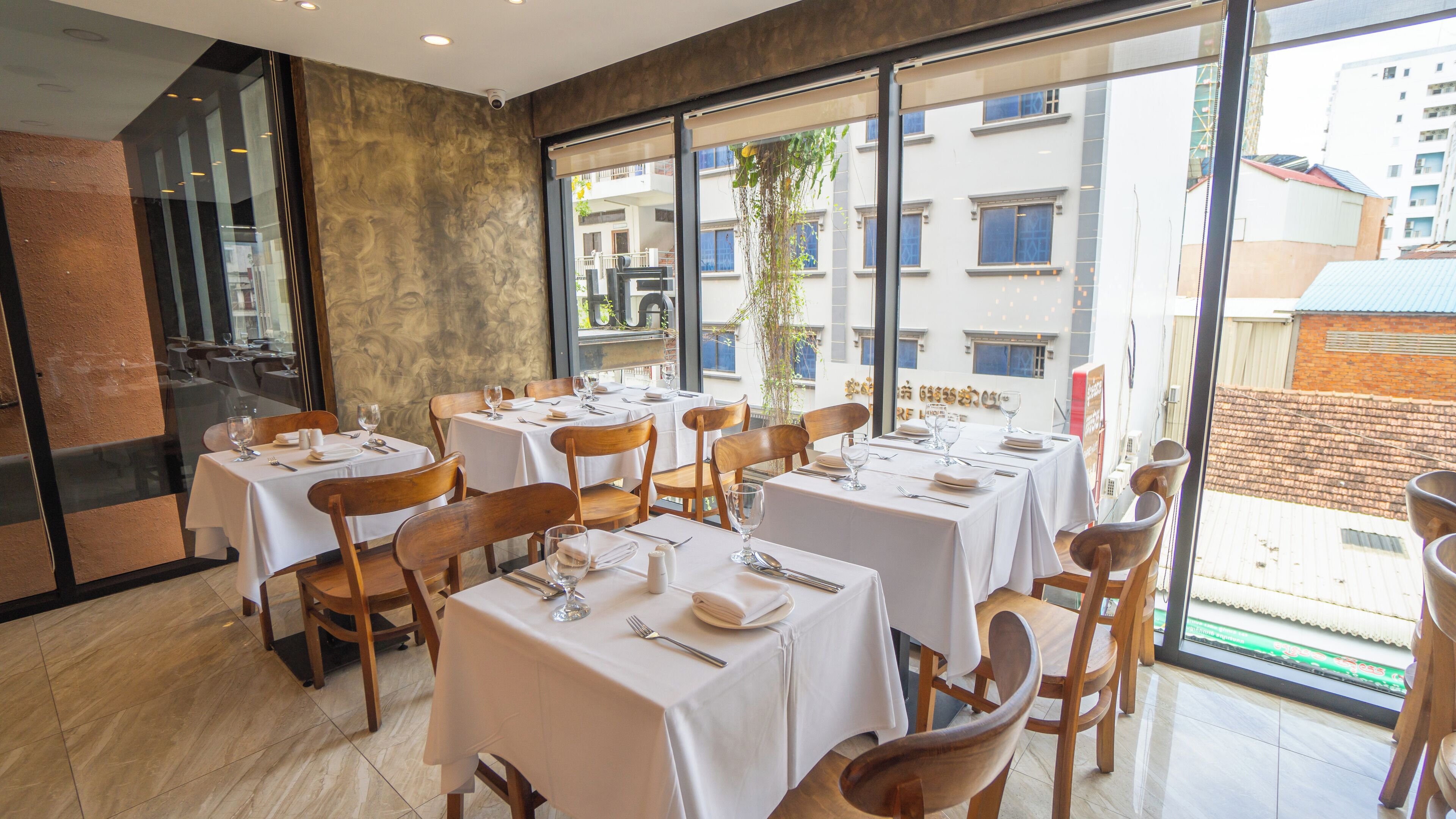 A restaurant with multiple tables set for dining, large windows offering a view of the city, and a modern interior design.