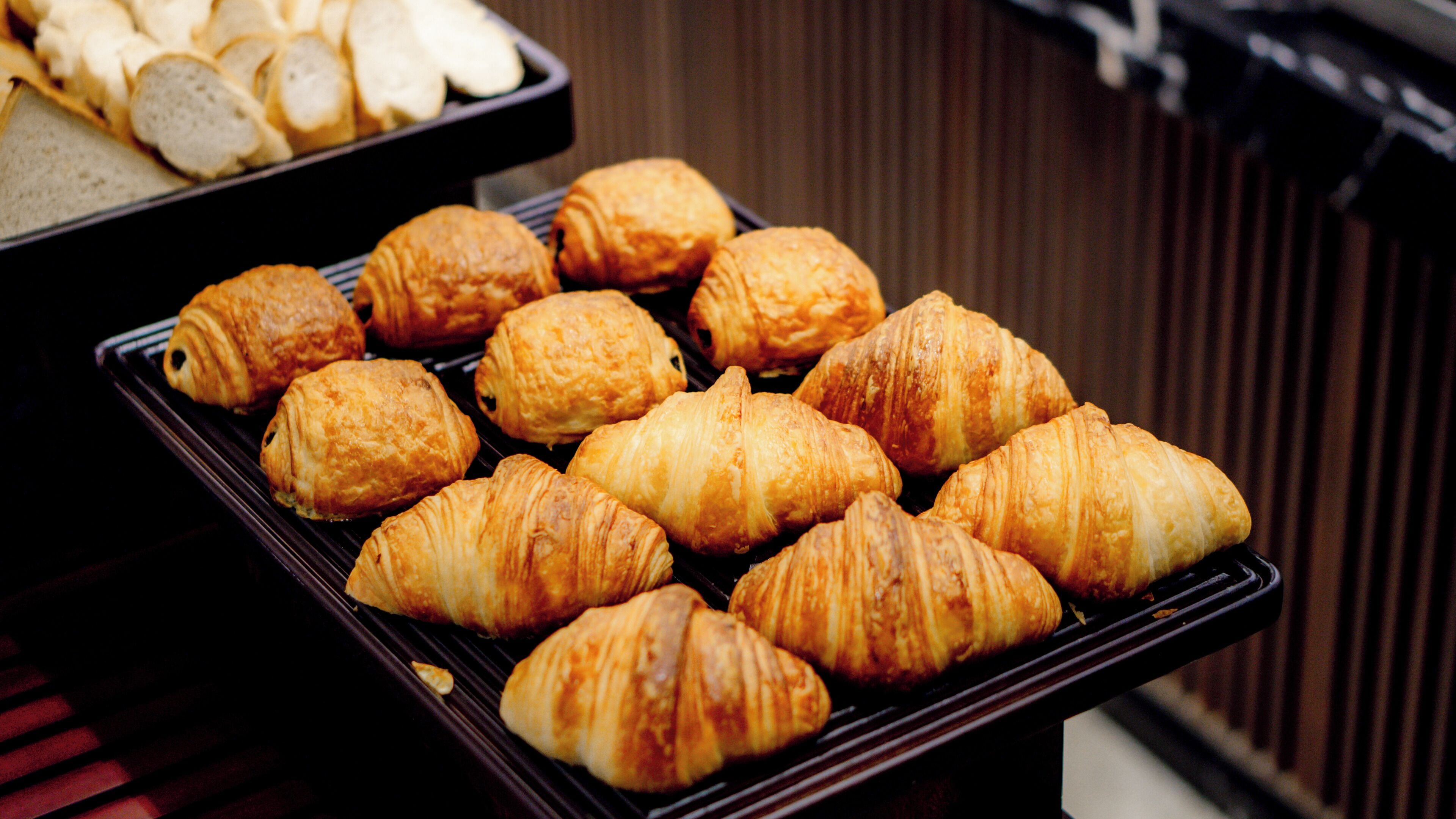Eine Auswahl an Gebäck auf einem Tablett, darunter Croissants und Brotscheiben, präsentiert auf einer Tischplatte.