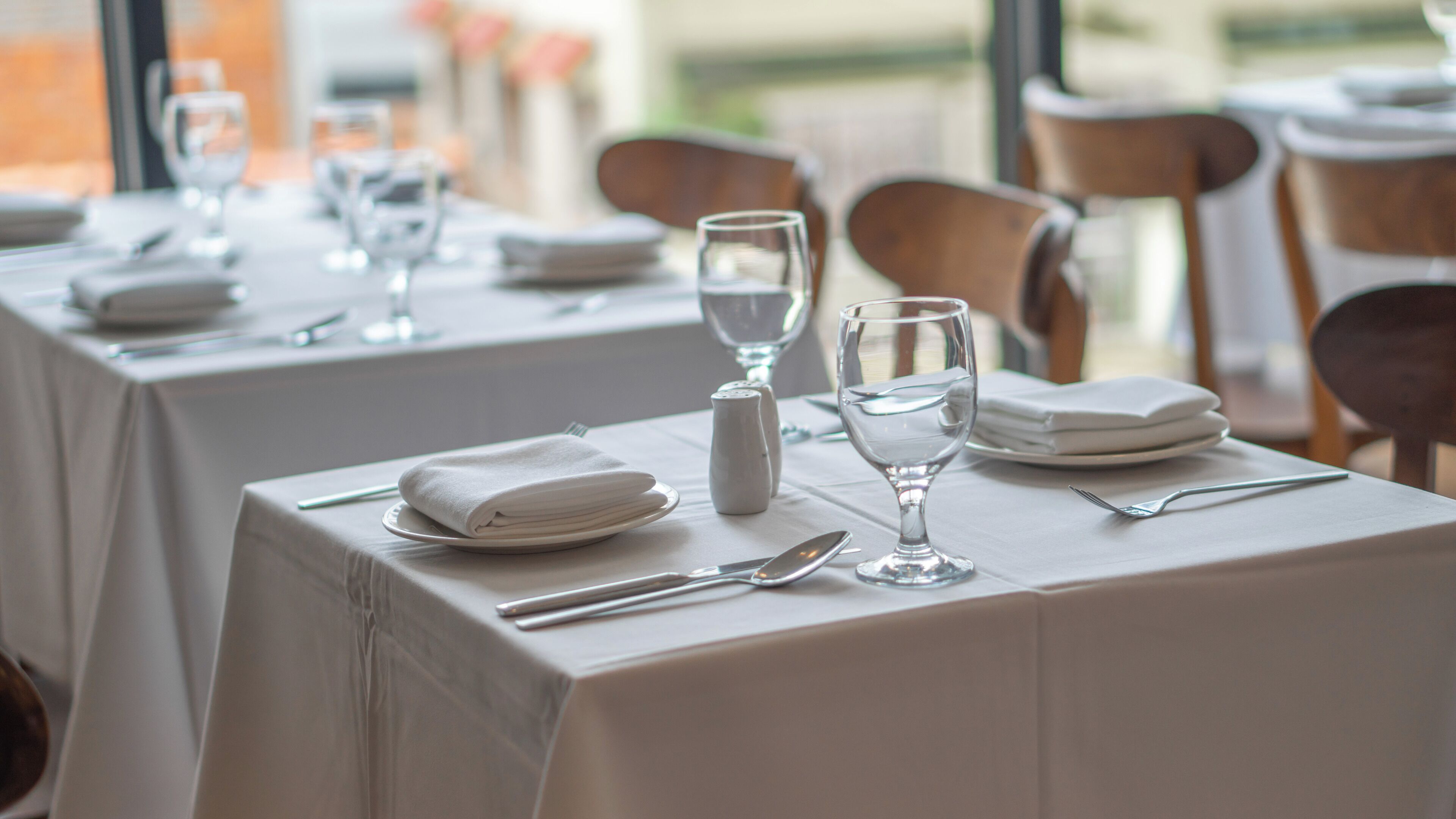 A dining table set with plates, cutlery, and glasses, covered with a white tablecloth.