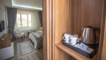 A hotel room with a wooden desk, a bed, a coffee maker, and a small table with a cup and a tissue box.