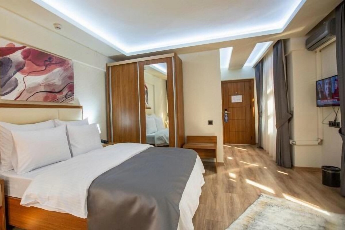 A hotel room with a bed, a nightstand, a TV, and a painting on the wall.