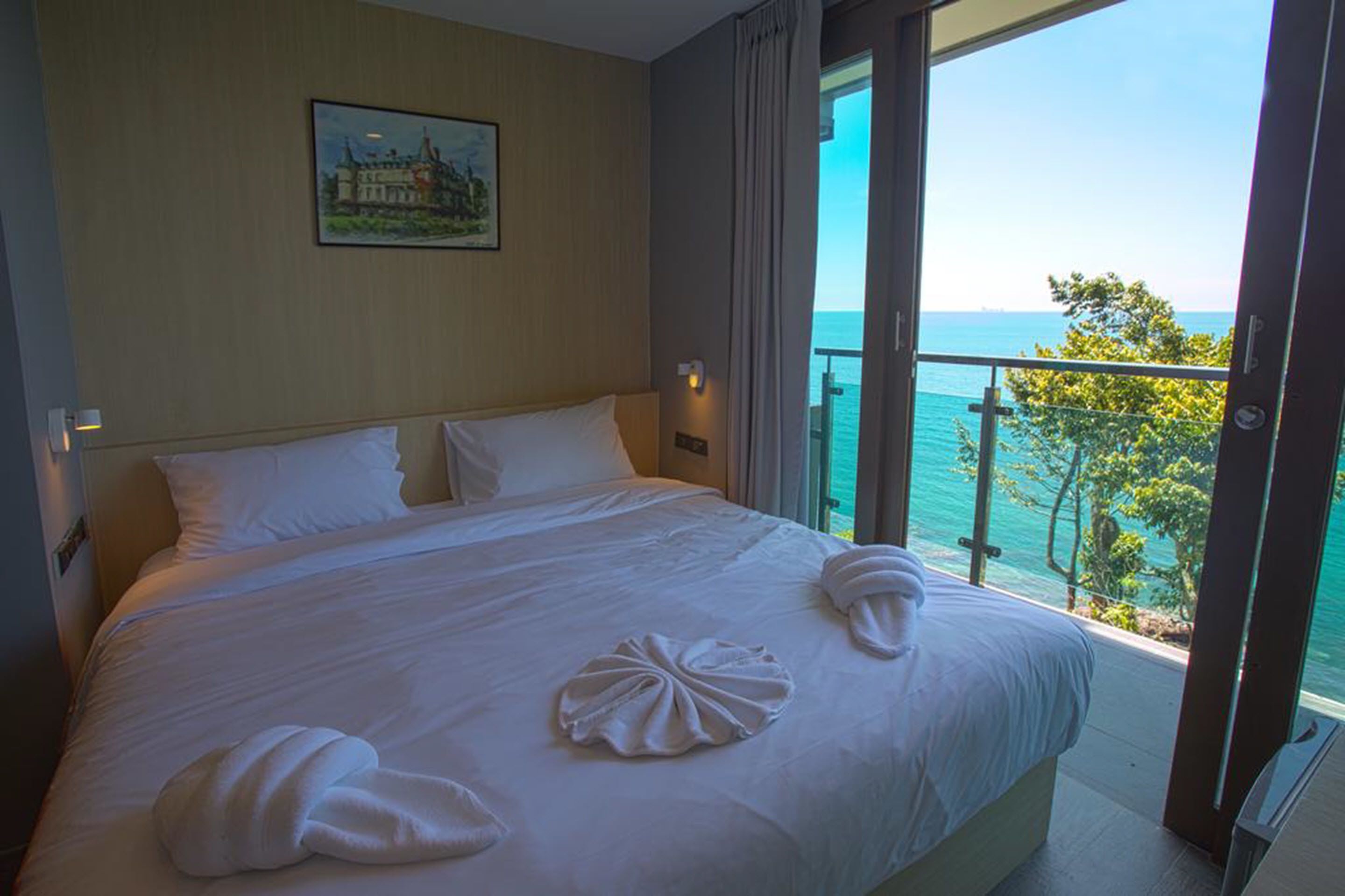 Ein Hotelzimmer mit einem großen Bett, einem Gemälde an der Wand und einem Balkon mit Meerblick.