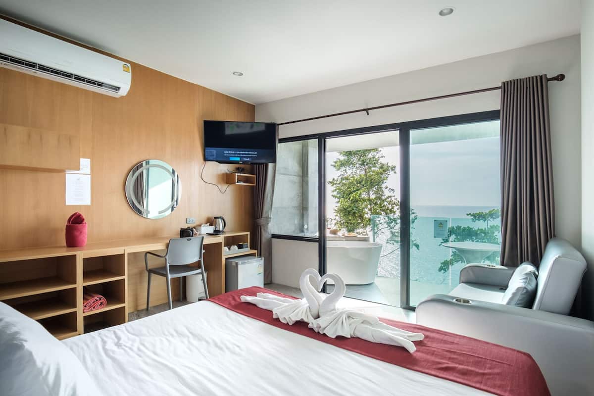 A modern hotel room with a bed, a desk, a chair, a television, and a large window with a view of the city.