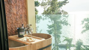 A wooden barrel with a wine bucket and glasses, a plate with food, and a view of trees and water. - Cliff Lanta Suite (Ko Lanta)