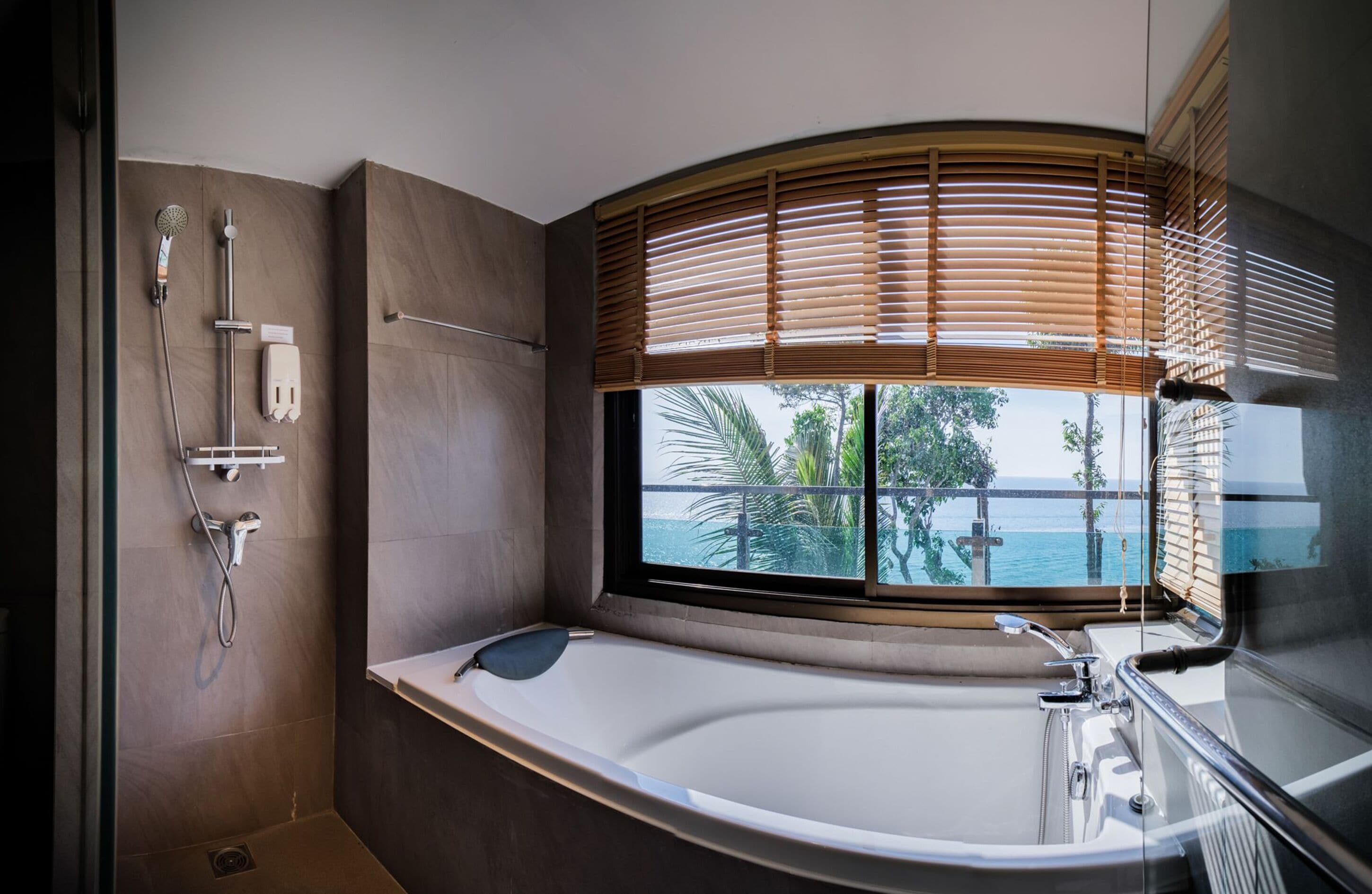 Un baño moderno con una bañera grande, una zona de ducha y una ventana con persianas.