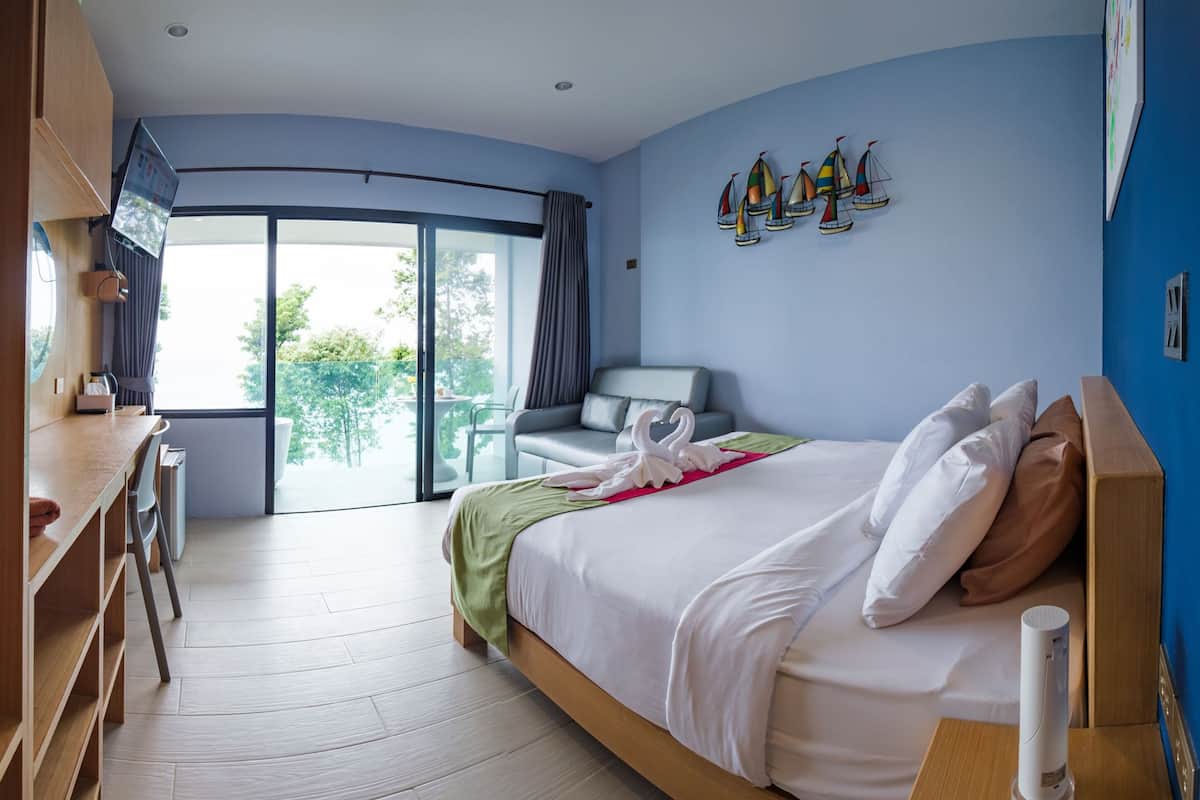 A modern hotel room with a large bed, a desk, and a balcony with a view.