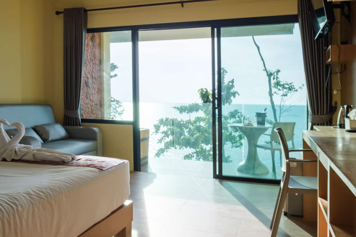 A modern hotel room with a bed, a desk, and a balcony with a view of the sea.