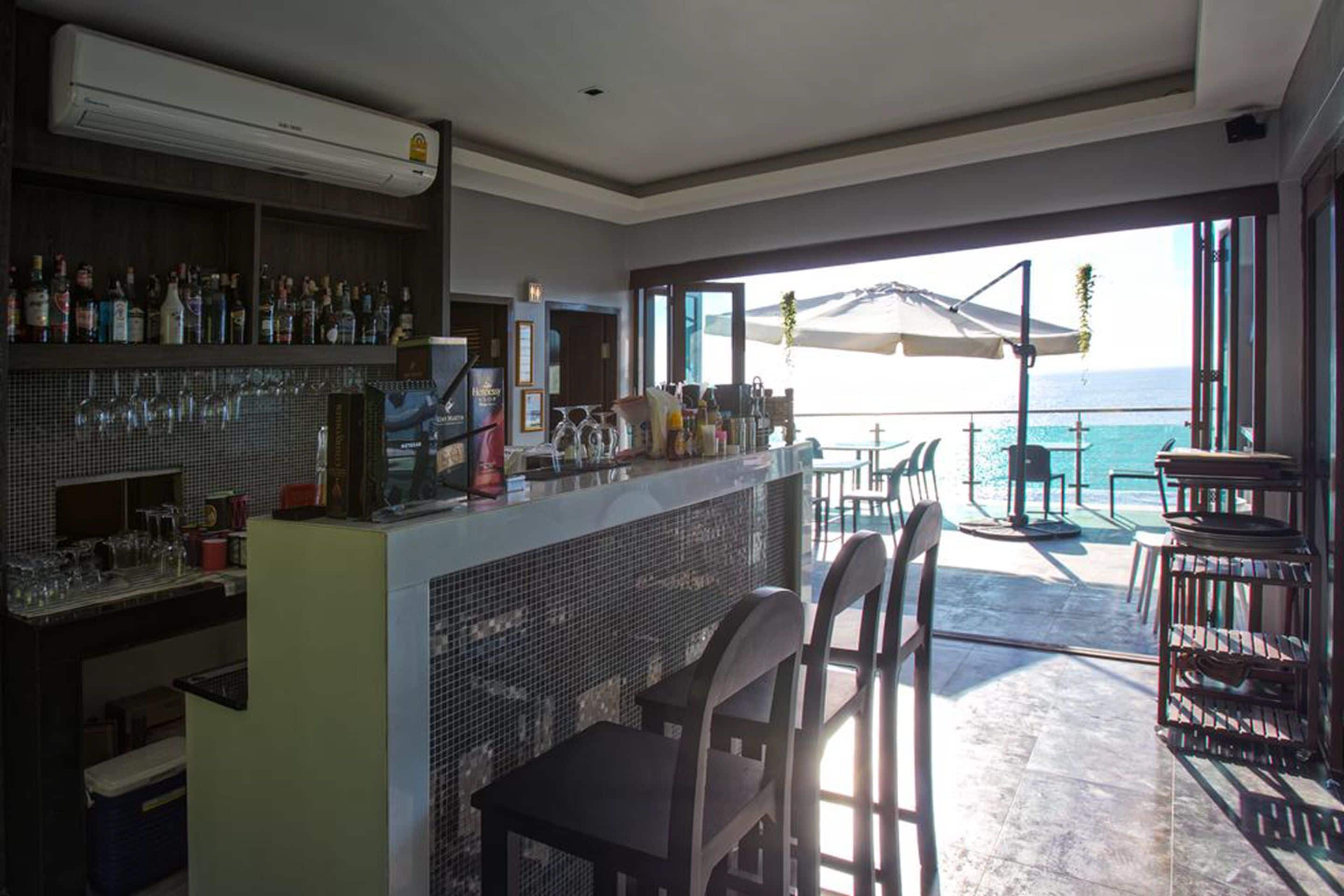 A bar area with a tiled backsplash, bar stools, and a view of the ocean through large windows.