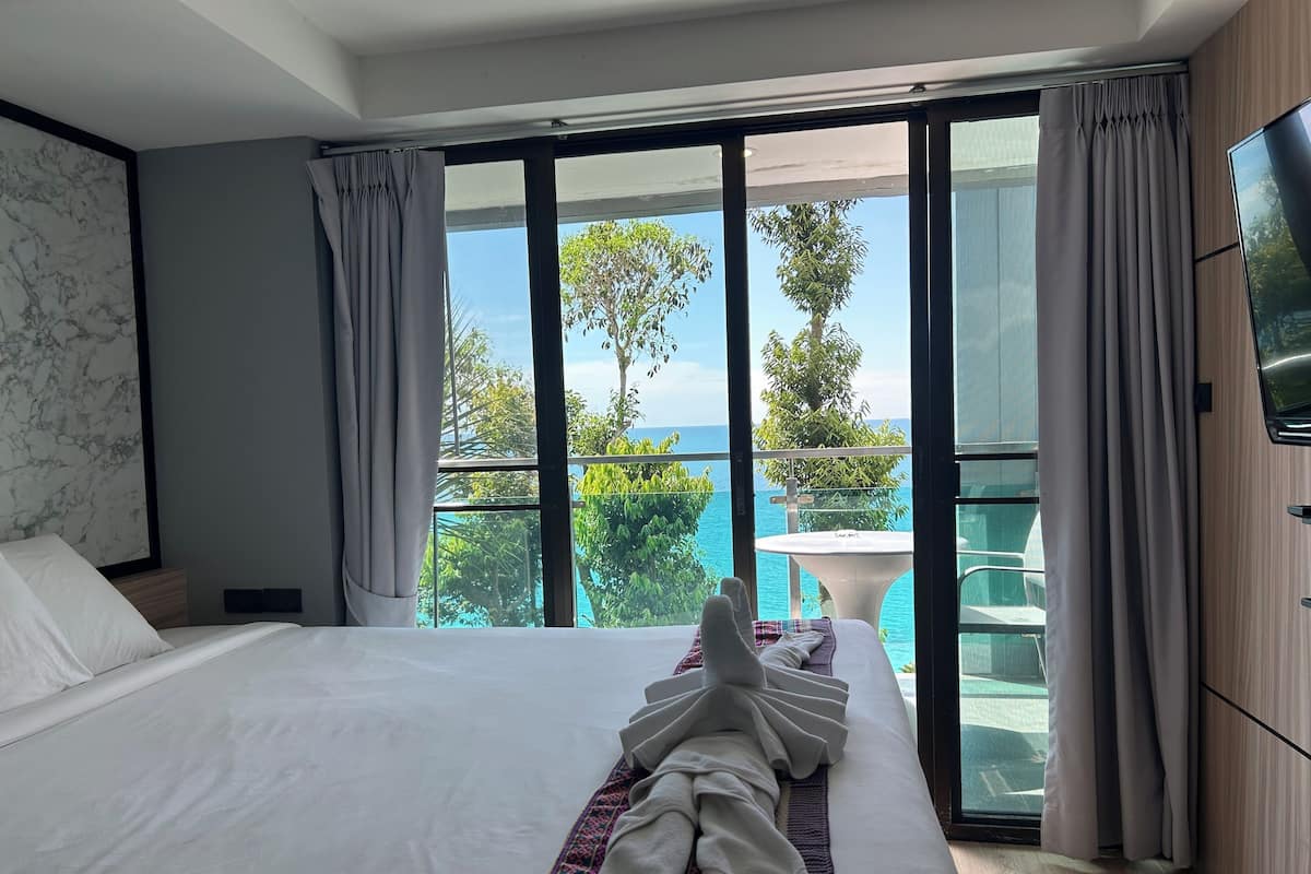 A hotel room with a large bed, a view of the ocean, and a balcony with a table and chairs.