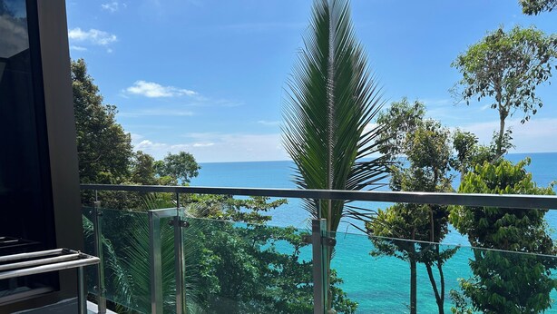 A balcony with a glass railing overlooking a turquoise sea and lush greenery. - Cliff Lanta Suite (Ko Lanta)