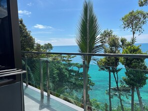 A balcony with a glass railing overlooking a turquoise sea and lush greenery. - Cliff Lanta Suite (Ko Lanta)