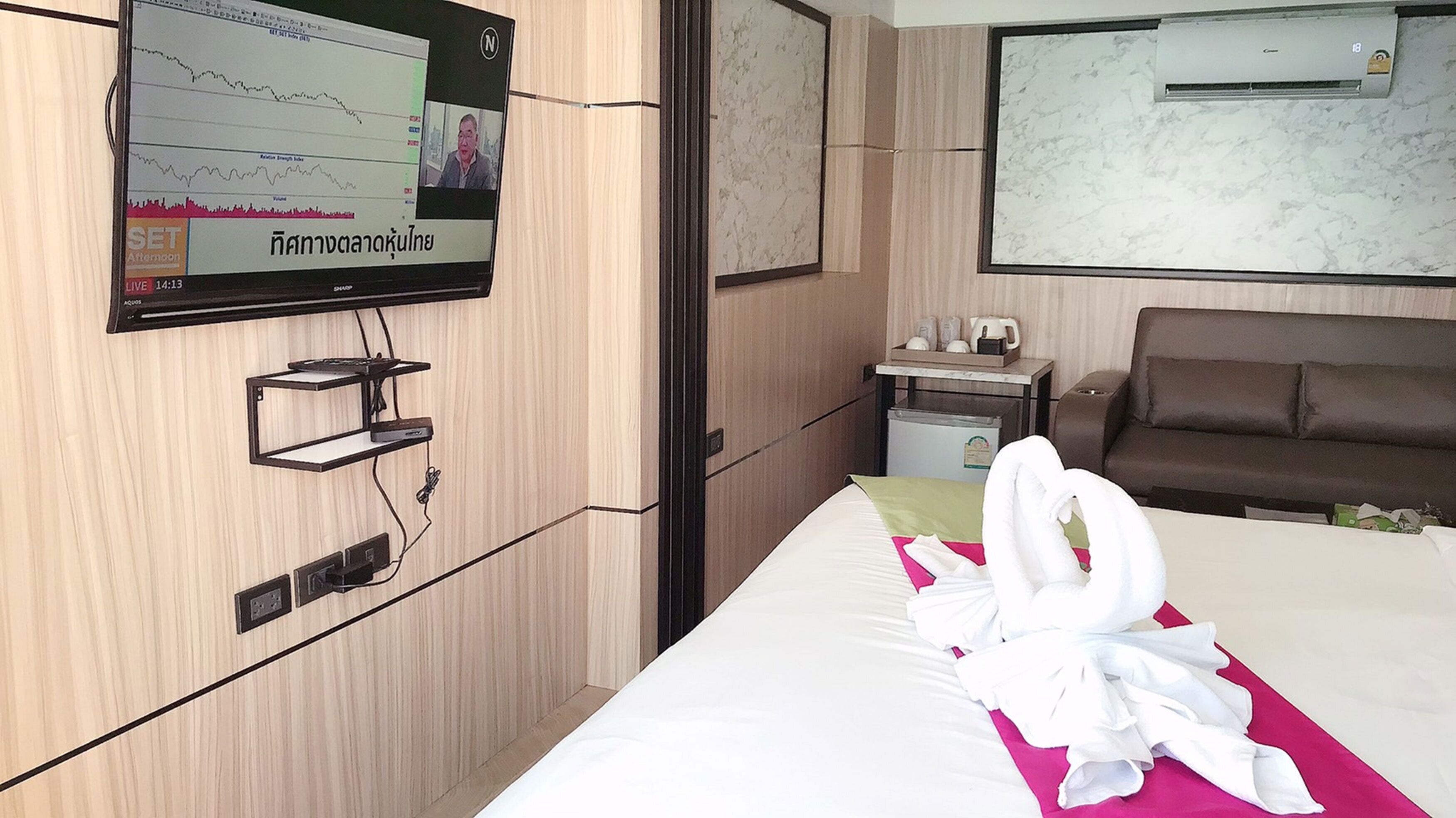 A hotel room with a bed, a TV mounted on the wall, a small table with a kettle, and a brown sofa.