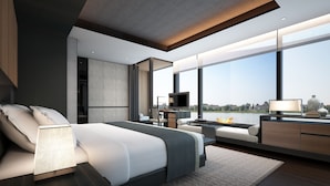 A modern bedroom with a large bed, a desk with a TV, and a view of a river.