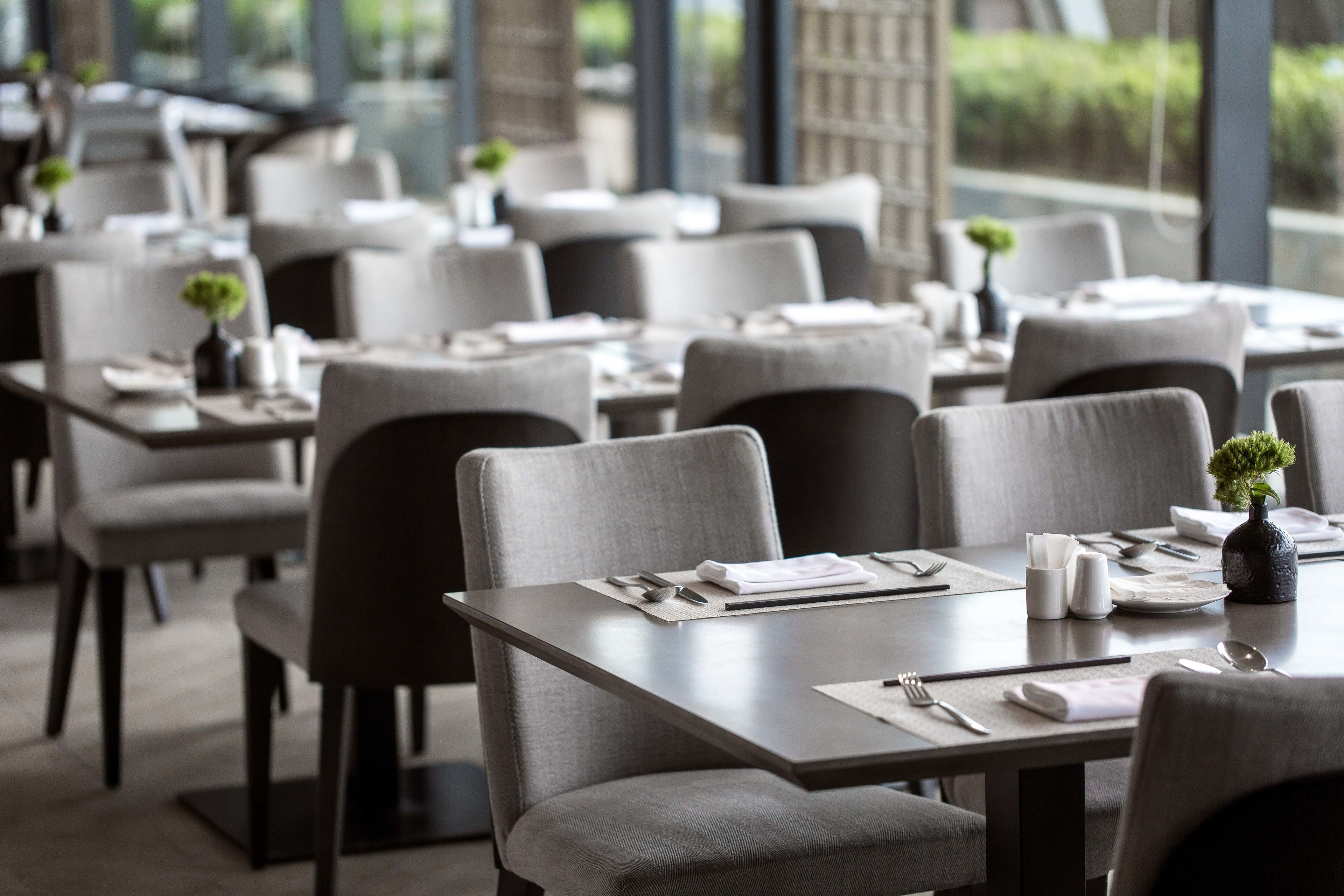 A restaurant with tables set for dining, chairs, and small potted plants on each table.