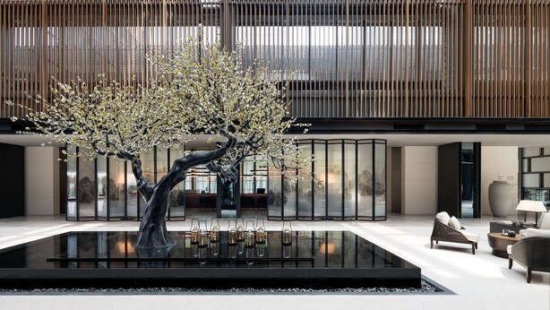 A modern lobby with a central black water feature, seating area, and a large glass partition.