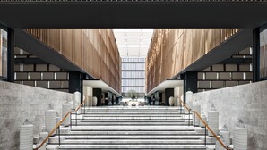 A modern building with a central staircase flanked by wooden slats and a glass ceiling.