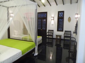 A room with a bed under a mosquito net, a chair, a small table, and a wall-mounted light fixture. - Saman Resort (Thissamaharama)