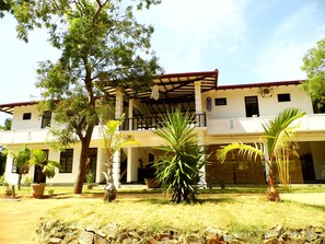 A two-story building with a covered patio area, surrounded by palm trees and potted plants. - Saman Resort (Thissamaharama)