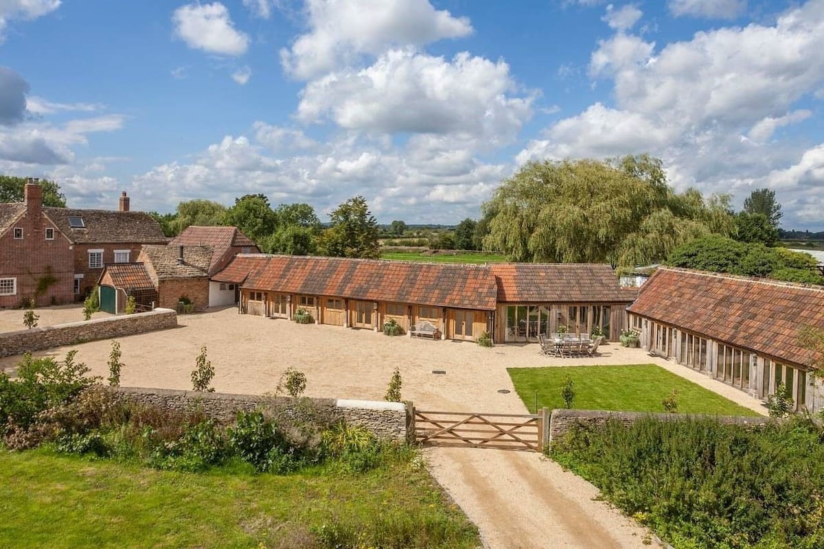A stable with multiple stalls, surrounded by a grassy area and a dirt path leading to a gate.
