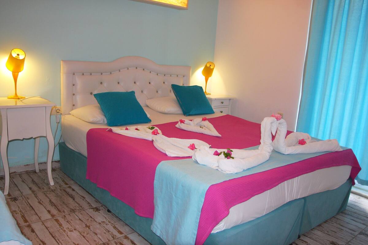 Ein ordentlich bezogenes Bett mit rosa und blauer Bettwäsche, zwei Kissen und einer dekorativen Handtuchgestaltung.