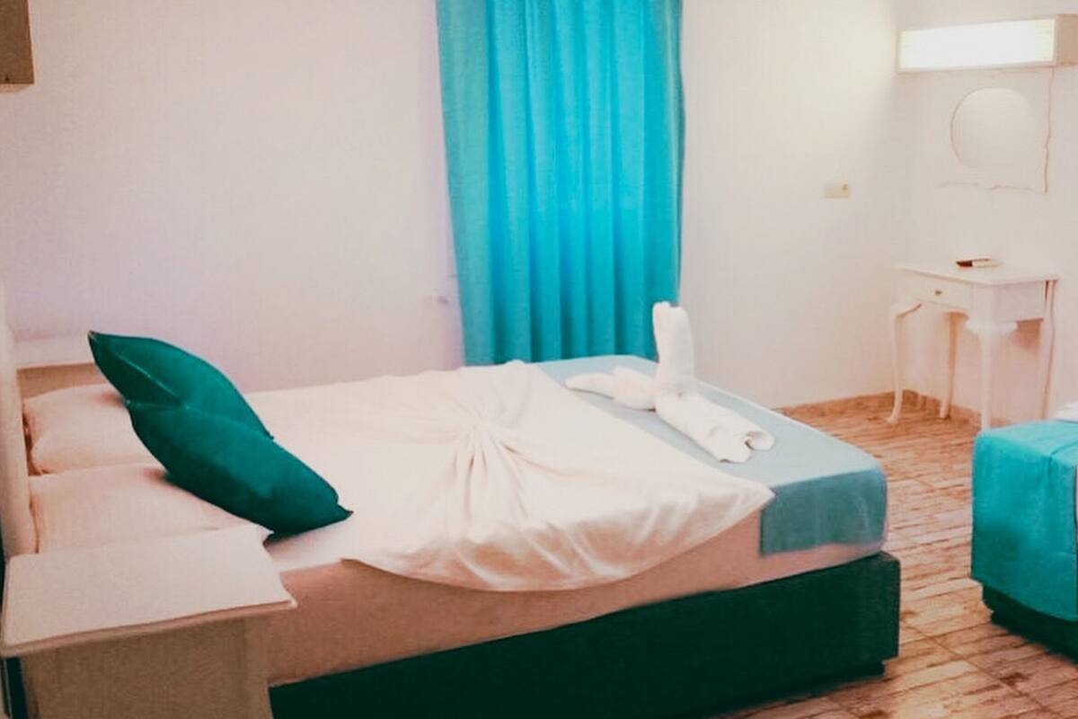 Ein Hotelzimmer mit Bett, einem kleinen Tisch, einem Spiegel und einem Fenster mit Vorhängen.