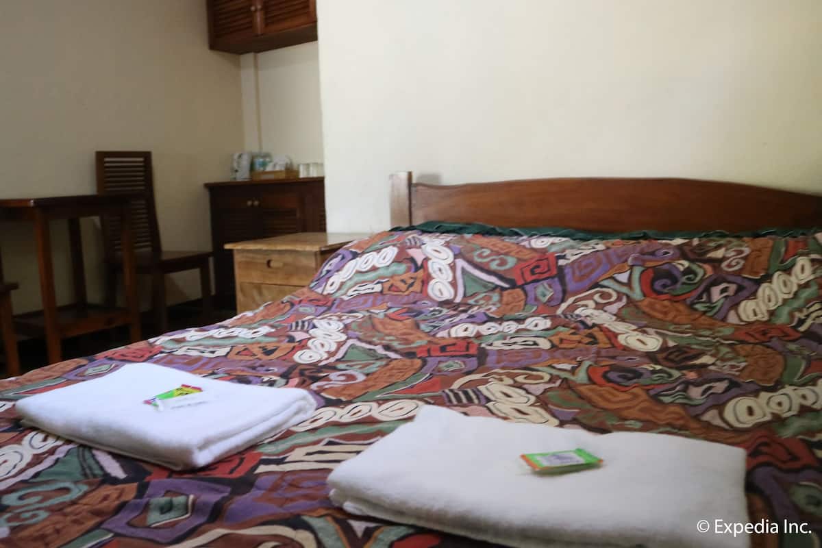 Quarto de hotel com uma cama, duas cadeiras, uma mesinha de cabeceira de madeira e um armário.