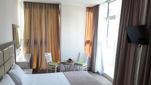 A hotel room with a large bed, two chairs, a small table with fruit, a TV, and curtains. - Hotel Green Glass (Batumi)