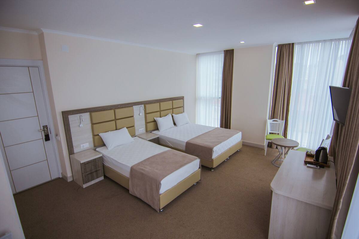 A hotel room with two beds, a desk, a chair, and a TV.